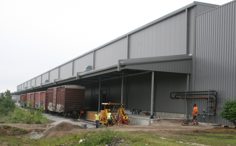 FIGURE 2. New Rail Siding Adjacent Expanded Warehouse 
This image shows four railroad boxcars positioned next to a loading dock along the side of a modern warehouse.
